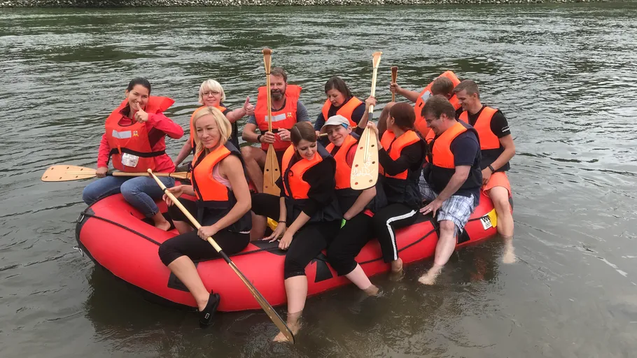 Menschen sitzen auf Floß mit Paddeln, Fluss im Hintergrund.