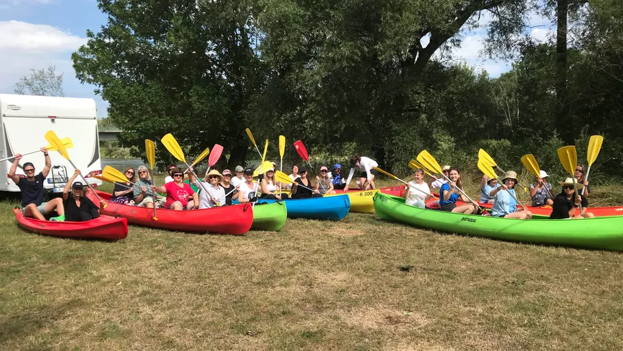 Gruppe in bunten Kajaks hält Paddel quer.