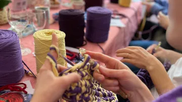 Hands knitting with yarns on a table.