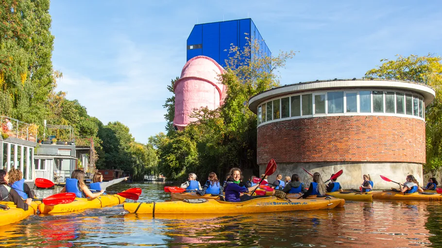 People kayaking on a canal with buildings.