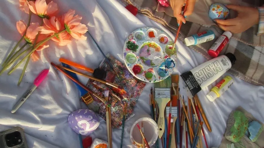 Person painting rocks, surrounded by art supplies.