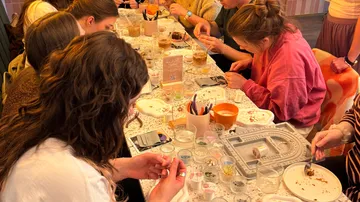 People crafting jewelry at a long table indoors.