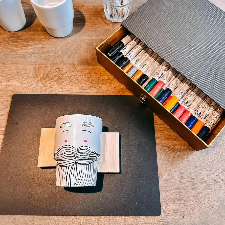 Decorated mug with markers in box on table.
