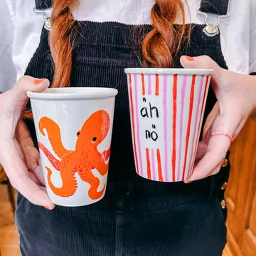 Person holding two mugs with designs.