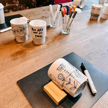 Decorated mugs and markers on wooden table.