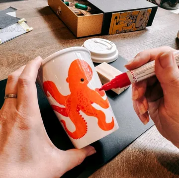 Hände zeichnen roten Oktopus auf weißem Becher.