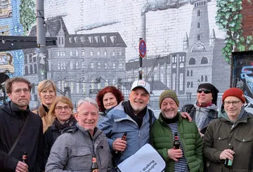 Gruppe von Menschen lächelt vor Wandgemälde.