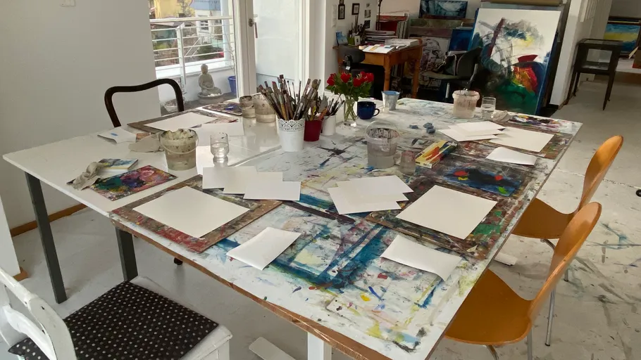 Art studio table with supplies and paintings.