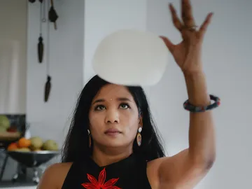 A woman throws up a ball of dough into a kitchen.