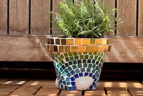 Mosaic pot with plant on wooden surface.
