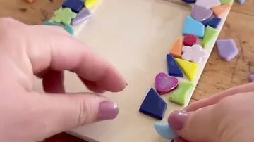 Hände legen bunte Fliesen auf einen Rahmen.