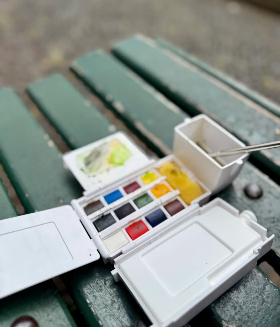 Watercolors set open on green bench.