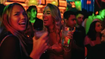 Zwei Frauen lachen und halten Getränke im Club.