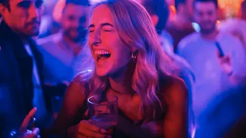 Frau lacht und hält ein Getränk im Nachtclub.