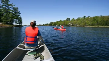 People canoeing on a calm lake under a blue sky.