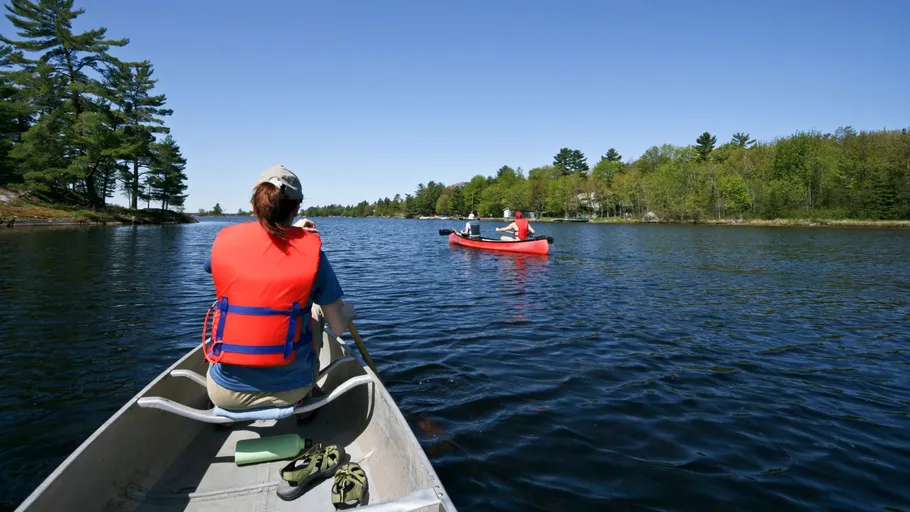 People canoeing on a calm lake under a blue sky.