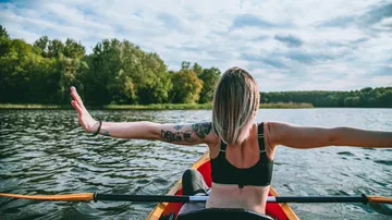 Frau im Kajak streckt Arme auf See.