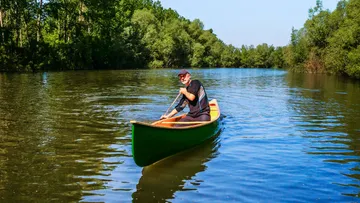 Mann paddelt grünes Kanu auf ruhigem Fluss.