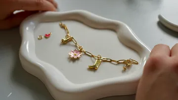 Gold bracelet with charms on white dish.