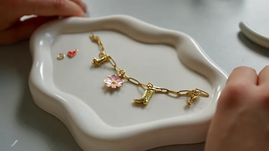 Gold bracelet with charms on white dish.