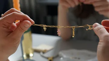 Hands holding gold charm bracelet indoors.