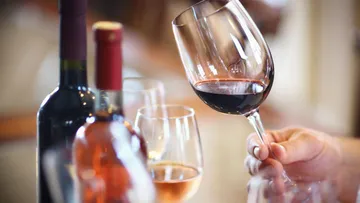 Person holding wine glass, other bottles nearby.