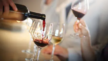 Wine being poured into a glass, people holding glasses.