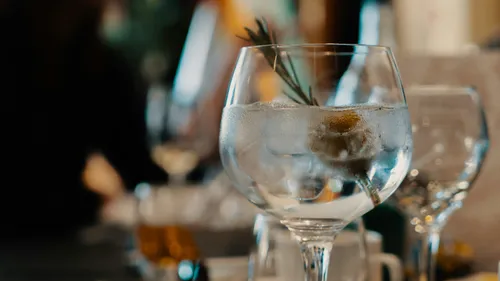 Cocktailglas mit Eis und Kräutern auf Tisch.