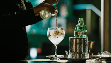 Barkeeper gießt Getränk in Glas mit Eis.
