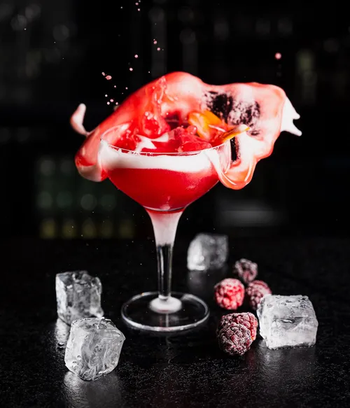 Red cocktail with splash, ice cubes, and berries.