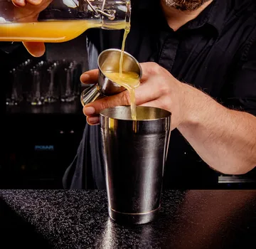 Bartender pouring juice into cocktail shaker.