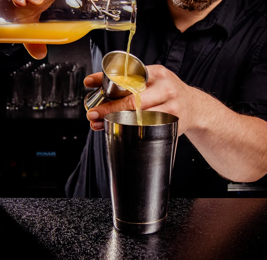 Barkeeper gießt Saft in Cocktailshaker.