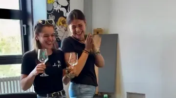 Zwei lachende Frauen mit Weingläsern im Innenraum.