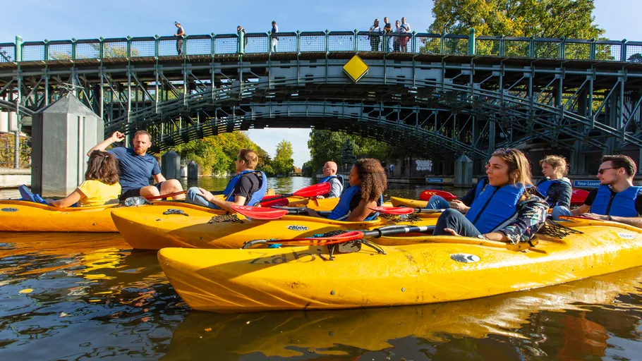 People kayaking on river, bridge above.