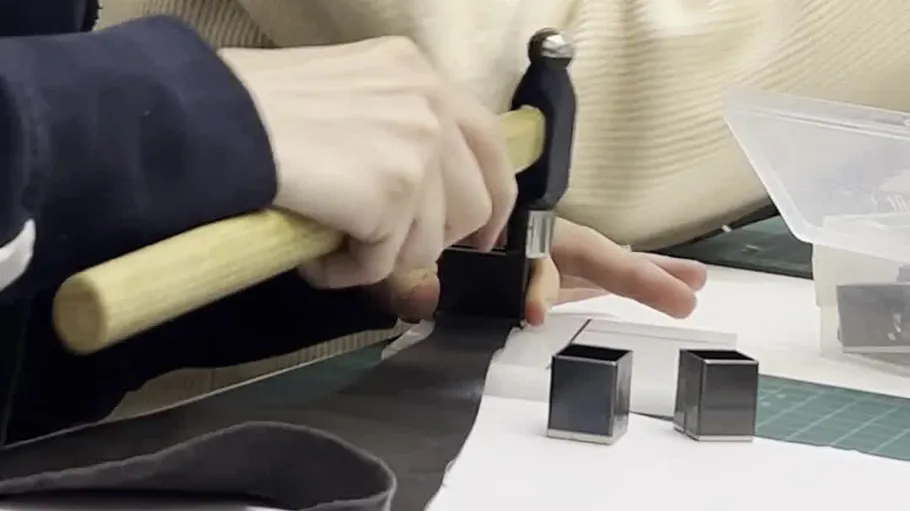 Person hammering tool on black fabric.