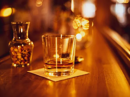 A glass of whiskey is sitting on a wooden counter.