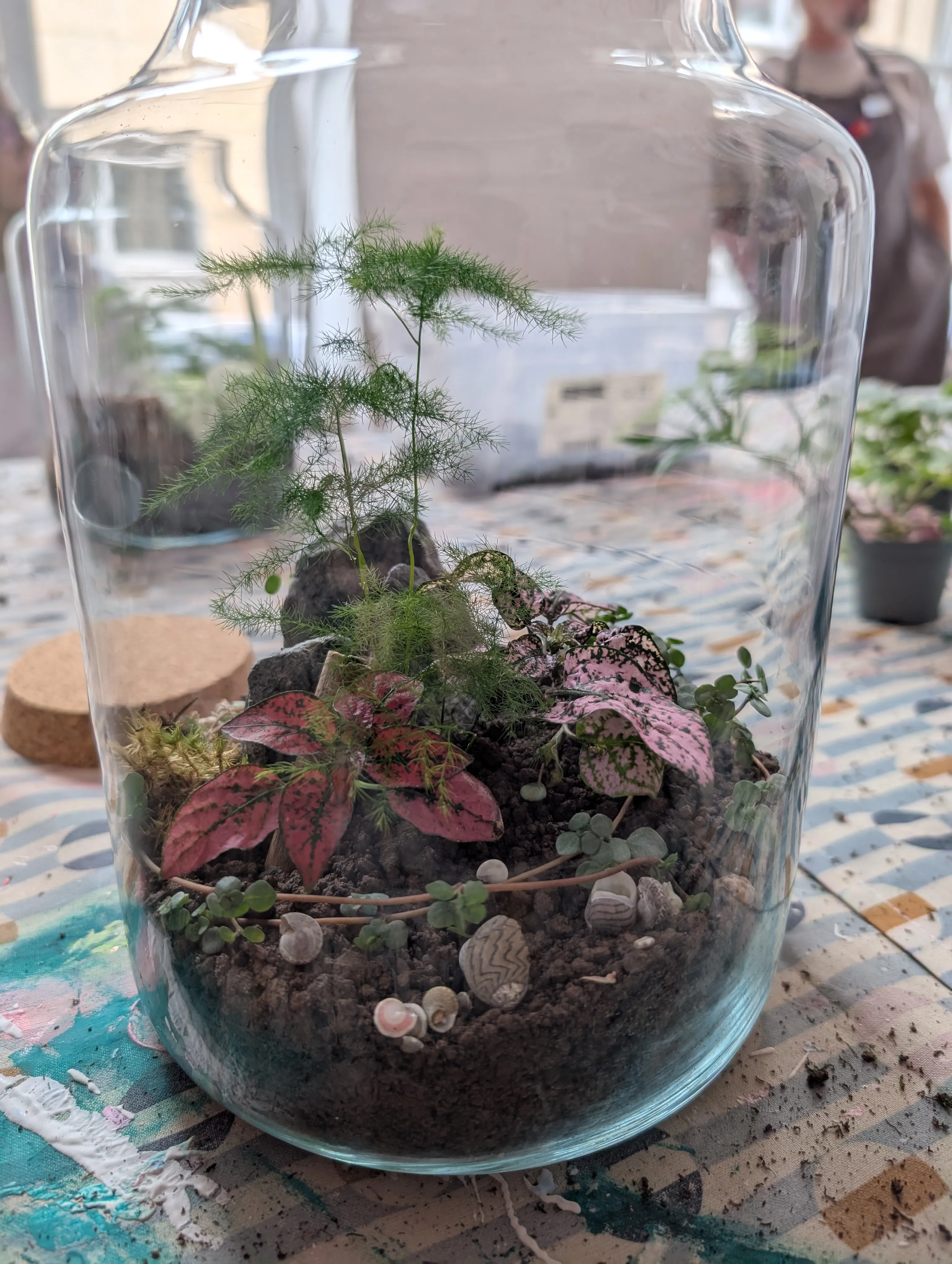 Glass jar with plants and soil on table.