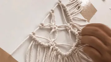 Hand knüpft Makramee-Knoten auf weißem Brett.