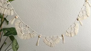Makramee-Girlande mit Quasten vor Wand.