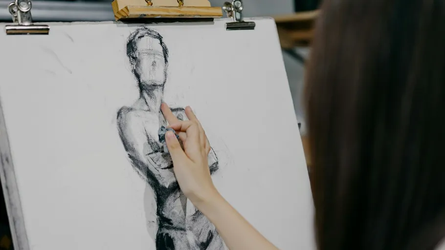 Person draws a charcoal figure on easel.