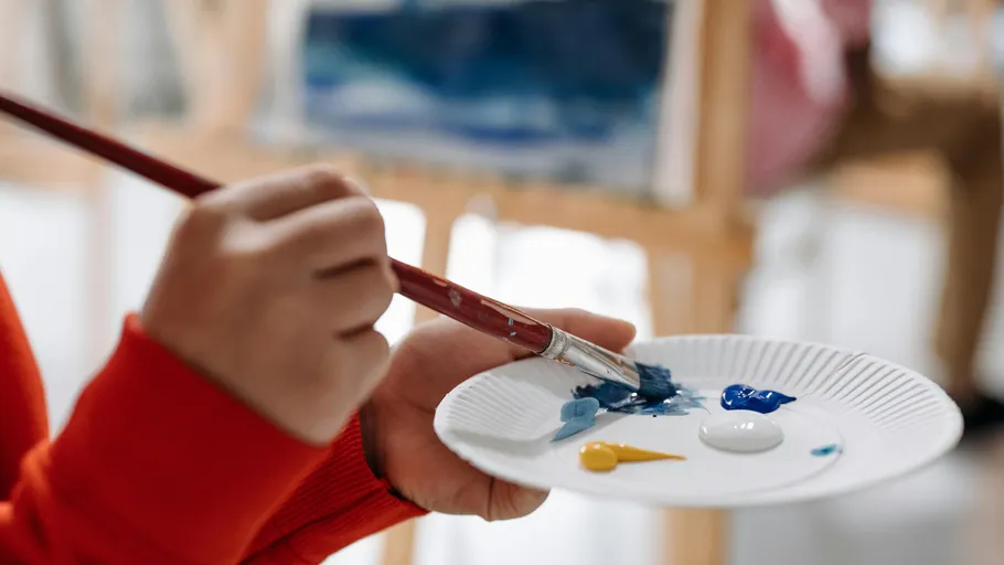 Person painting with brush and palette indoors.