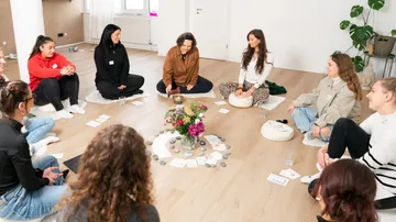 Gruppe sitzt im Kreis um Blumen drinnen.