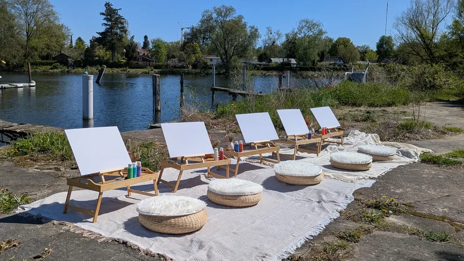 Easels and cushions by a lakeside on a sunny day.