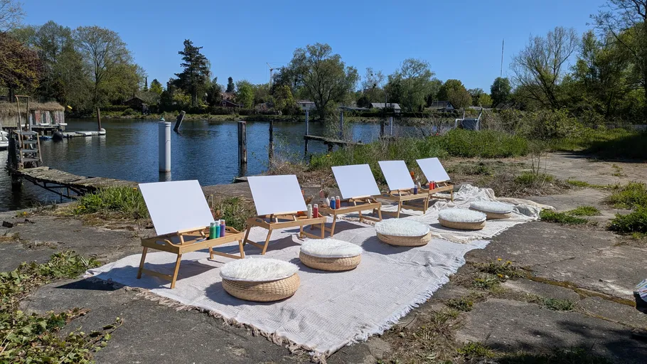 Easels and cushions by a lakeside on a sunny day.