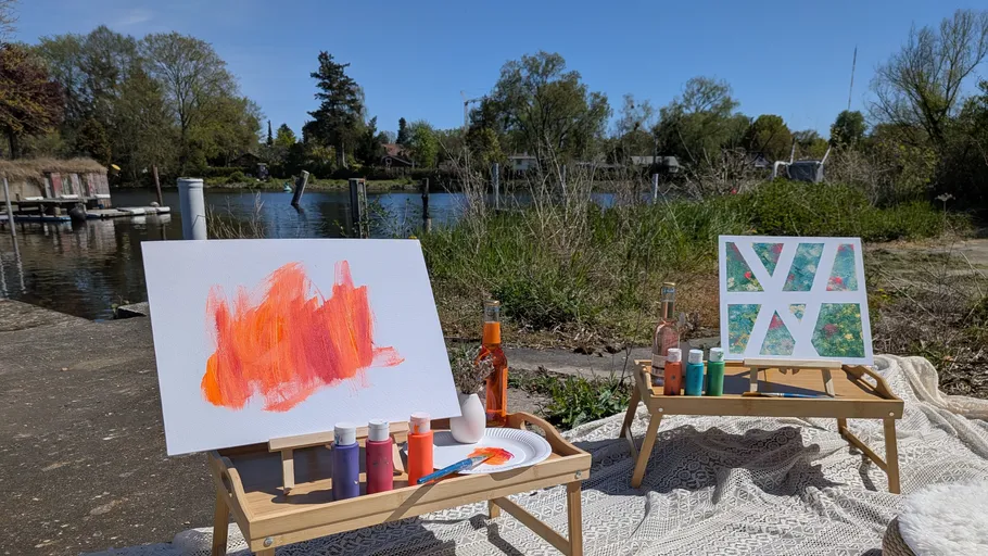 Two easels with paintings beside a lake.