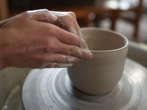 Hands shaping clay bowl on pottery wheel.