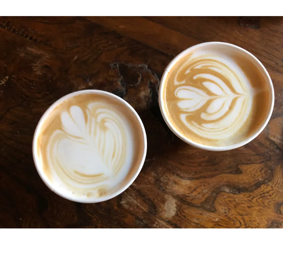 Two lattes with art on wooden table.