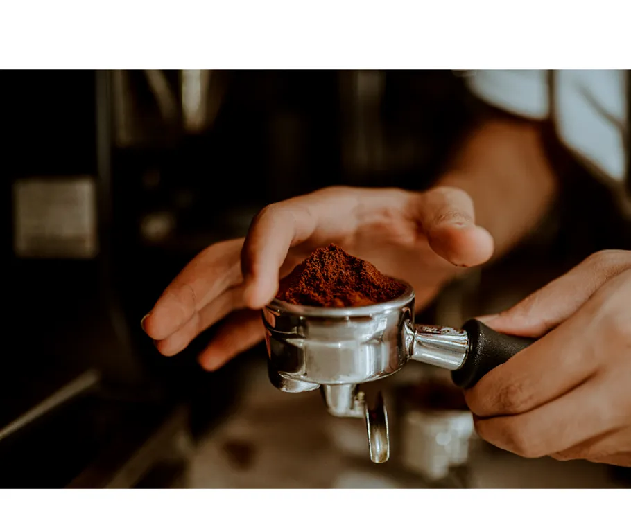 Hände halten Siebträger mit gemahlenem Kaffee.