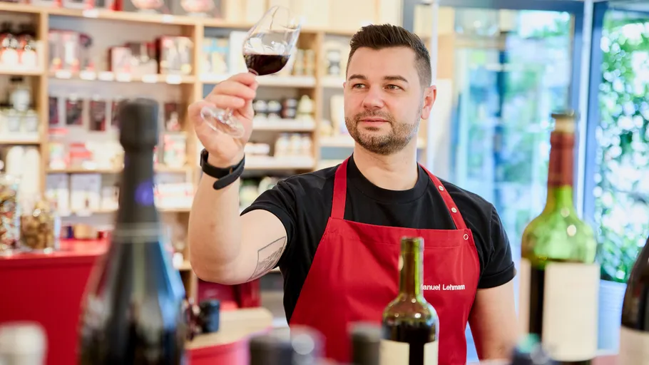 Man in red apron examining wine glass indoors.