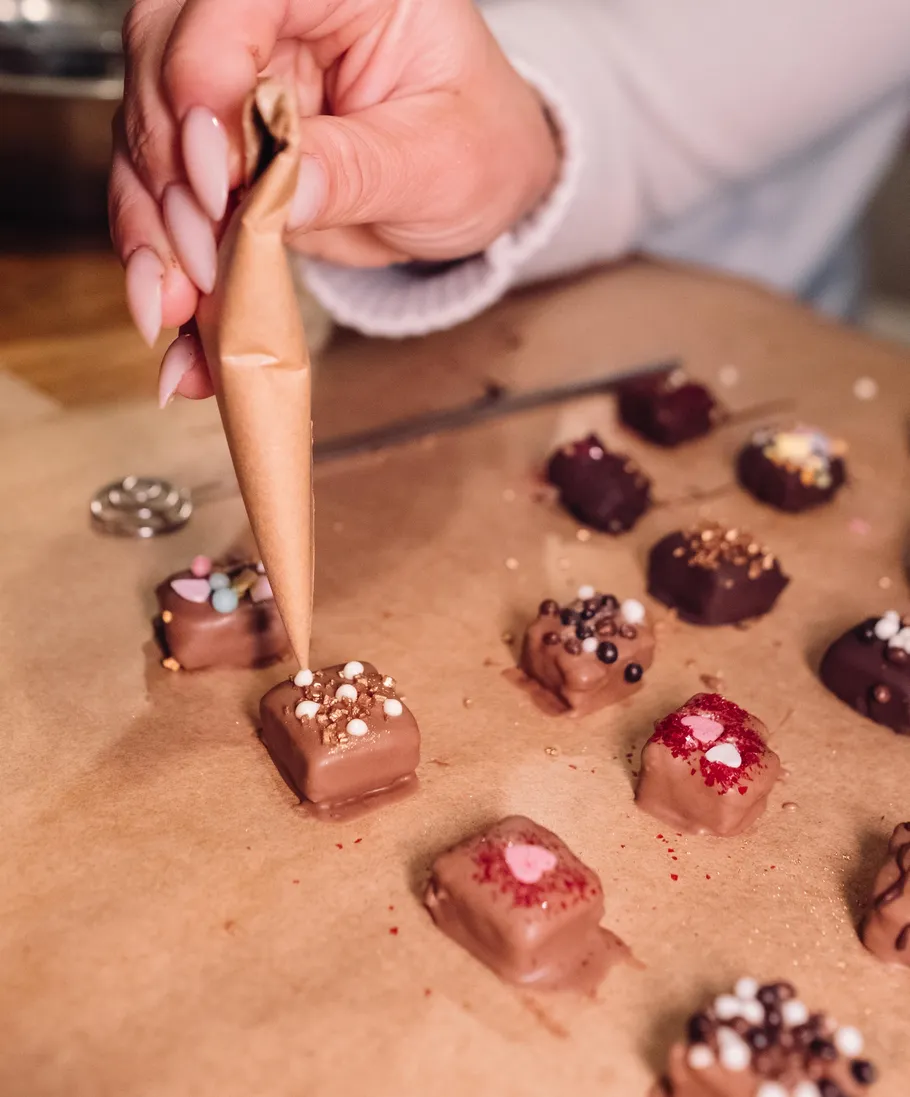 Person verziert Pralinen mit Zuckerguss auf Pergament.